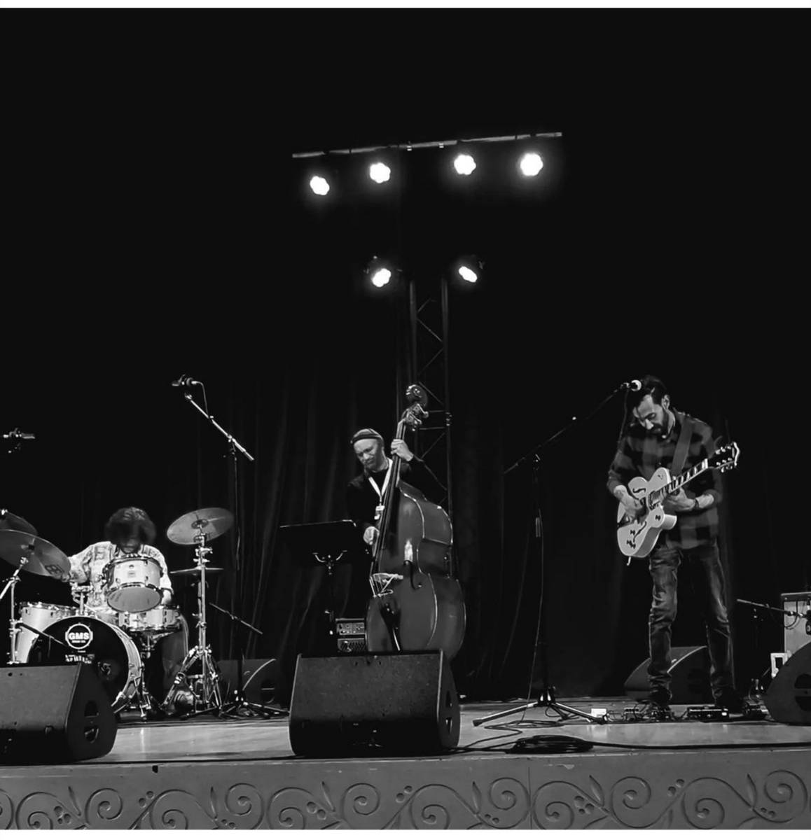 The trio performing live on stage — drums, double bass and guitar