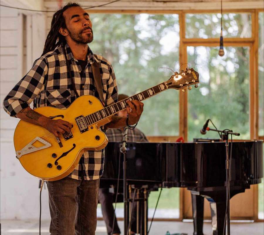 Amine playing guitar beside a grand piano